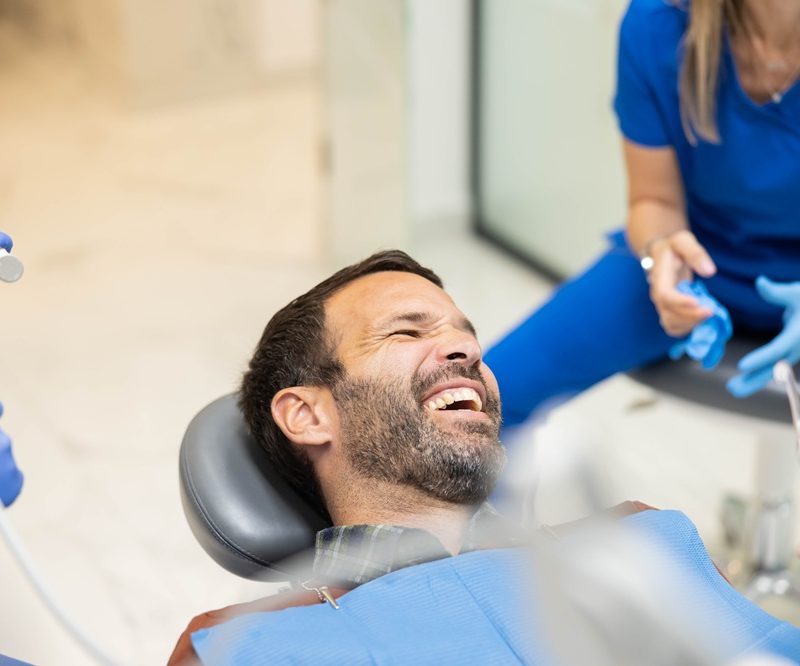 Male patient smiling and laughing in a dental chair while dental team prepares tools, highlighting a comfortable and friendly experience at DC Pearls Dental Boutique - ny dental boutique reviews