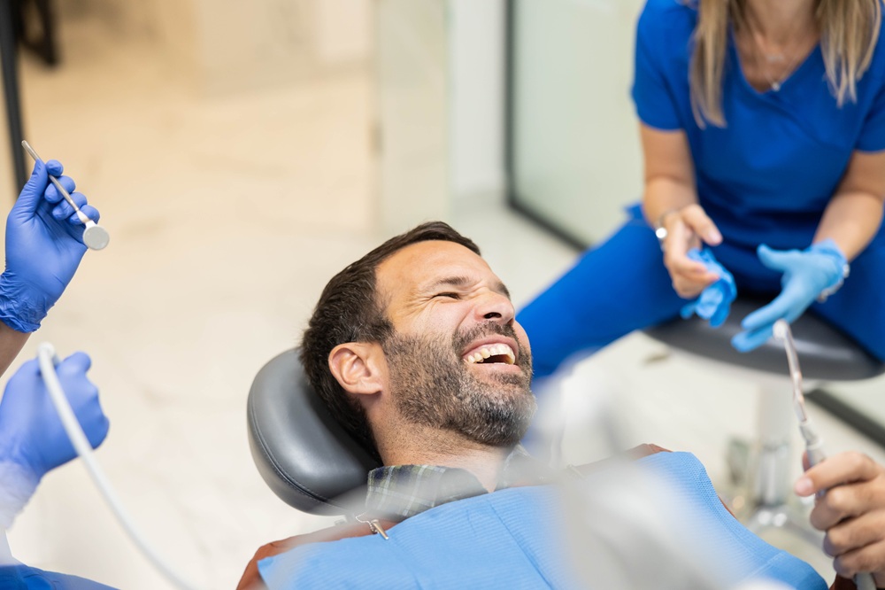 Relaxed Patient Smiling During Dental Visit - ny dental boutique reviews Male patient smiling and laughing in a dental chair while dental team prepares tools, highlighting a comfortable and friendly experience at DC Pearls Dental Boutique - ny dental boutique reviews