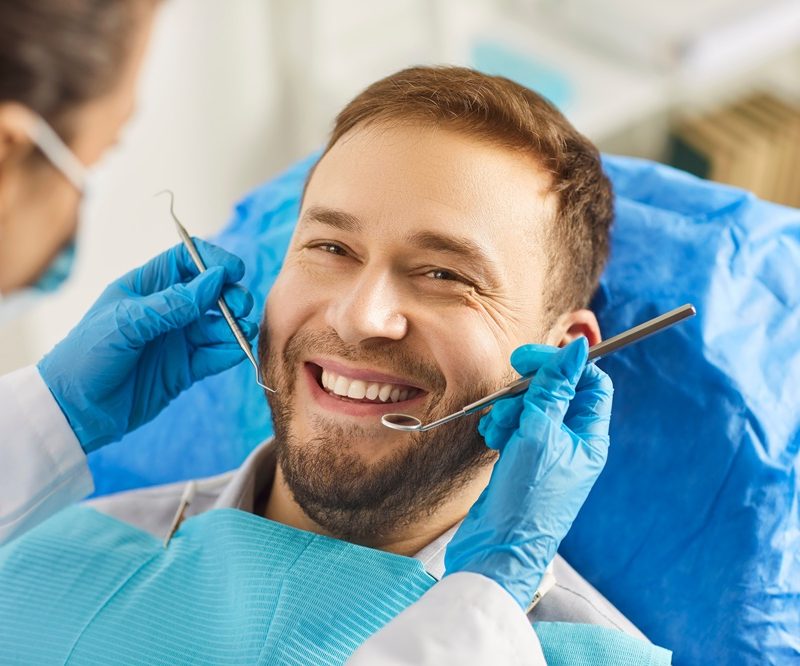 Smiling male patient in dental chair during treatment, highlighting improved confidence and aesthetic results from a smile makeover - Benefits of Smile Makeover