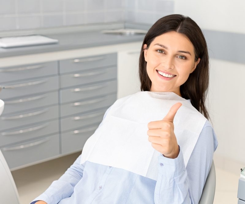 Portrait of pretty brunette female patient smiling and showing thumb up in dentistry, free space