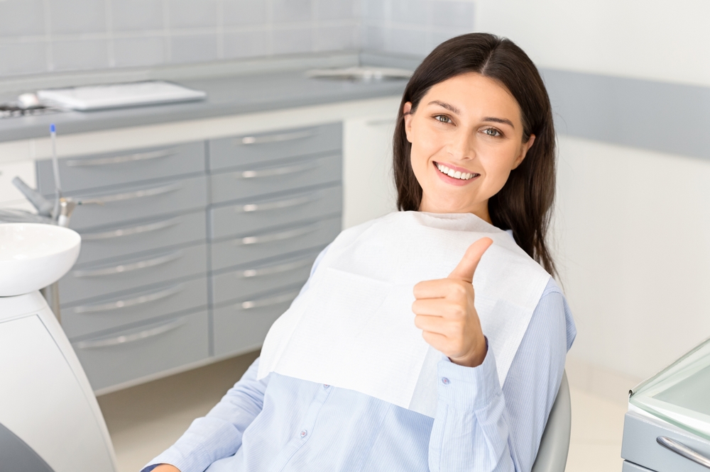 Portrait of pretty brunette female patient smiling and showing thumb up in dentistry, free space
