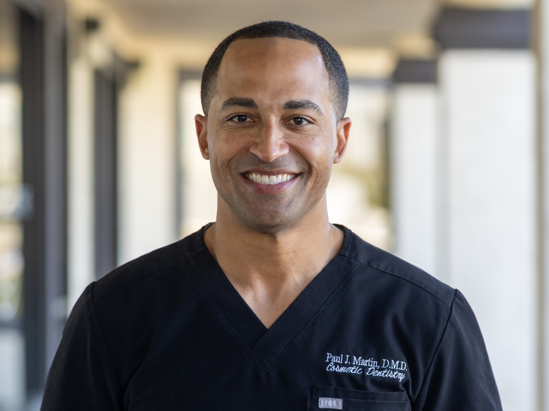 Portrait of Dr. Martin in black scrubs smiling with arms crossed in a modern office setting, representing a trusted dentist in Hillcrest San Diego - Dentist Hillcrest San Diego