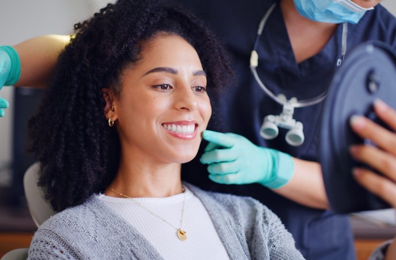 Woman, smile and mirror for checkup with dentist, oral hygiene and mouth cleaning service. Female person, assessment and orthodontic inspection for dental care, patient and help for consultation