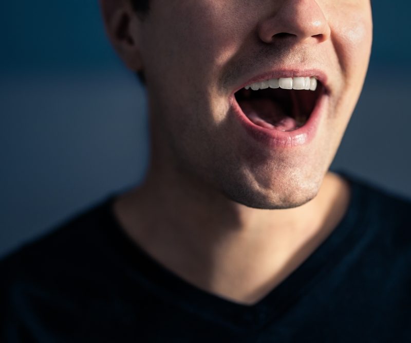 Close-up of a person with mouth open showing tongue and teeth, representing oral hygiene and the benefits of using a tongue scraper - Is a Tongue Scraper Good