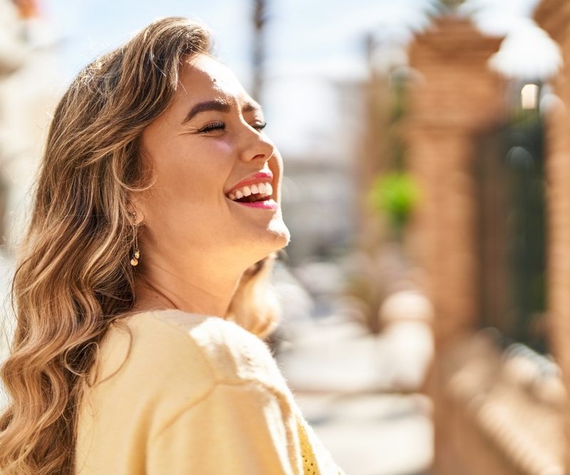 Woman smiling brightly in a sunny outdoor setting, showcasing a healthy, radiant smile and confidence from dental care at Signature Smiles Woodlands TX - Signature Smiles Woodlands TX