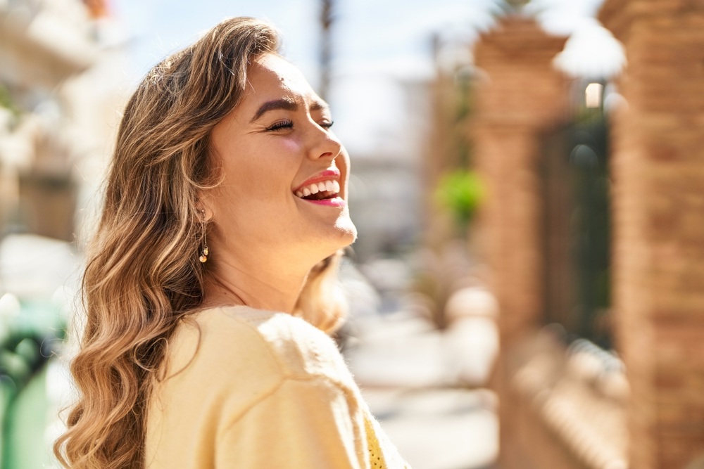 Confident Woman Smiling Outdoors with Bright Teeth - Signature Smiles Woodlands TX Woman smiling brightly in a sunny outdoor setting, showcasing a healthy, radiant smile and confidence from dental care at Signature Smiles Woodlands TX - Signature Smiles Woodlands TX